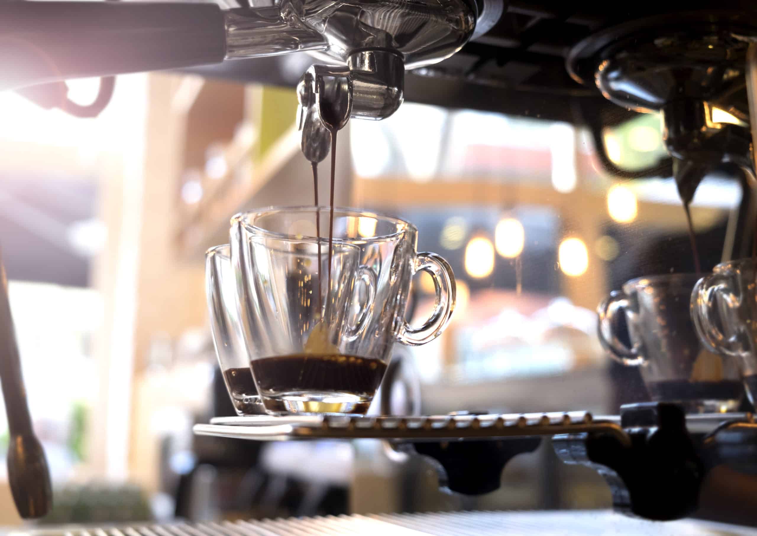 Genomskinlig kaffemugg som fylls med dryck i espressomaskin.